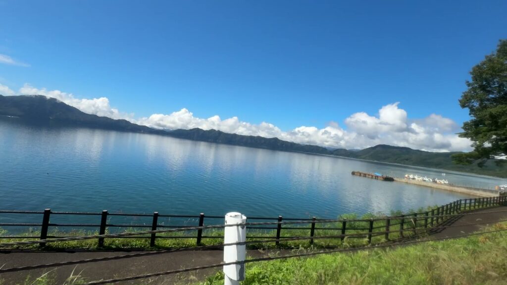 コーンが並ぶ湖沿いの直線と青い田沢湖