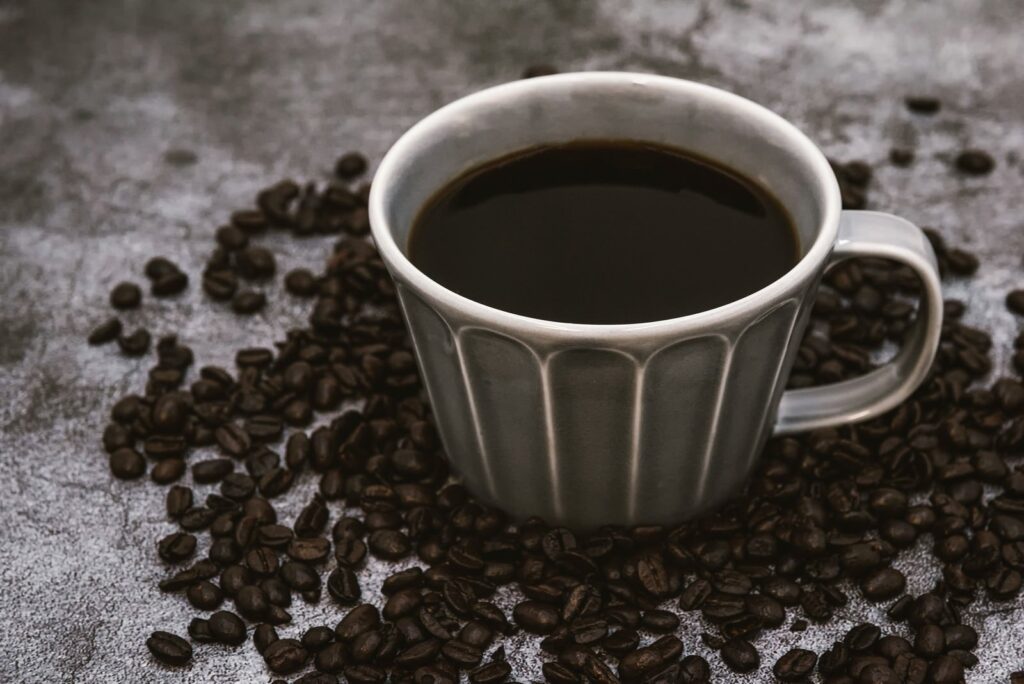 カップに注がれたブラックコーヒーと散らばったコーヒー豆