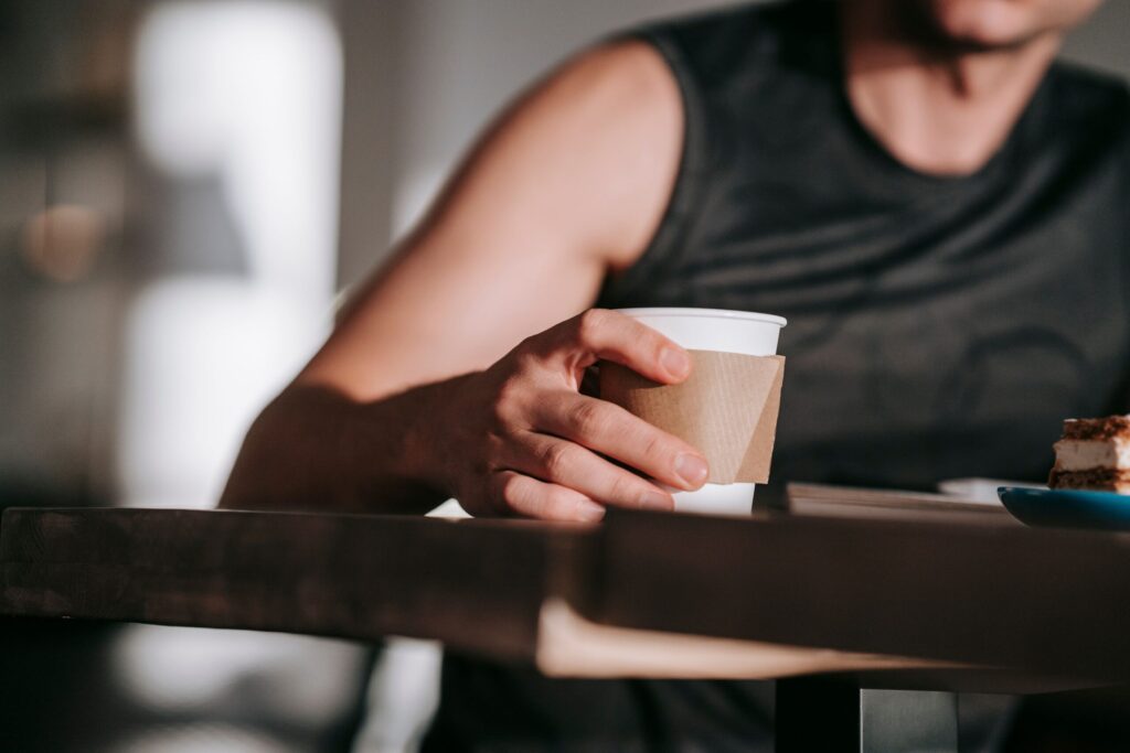 タンクトップ姿の男性がコーヒーカップを手に持っているところ